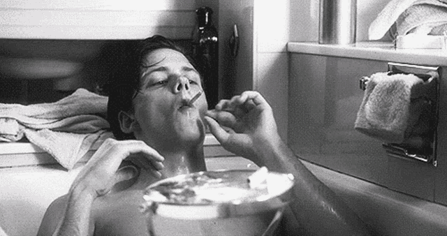 a man is sitting in a bathtub smoking a cigarette and drinking water .