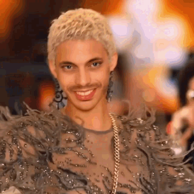 a man with blonde hair and a fake mustache is wearing a feathered dress and earrings .