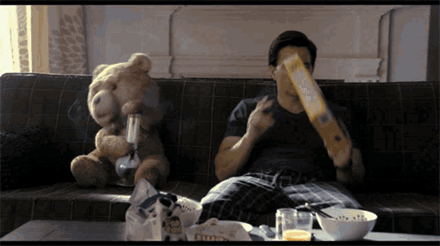a man is sitting on a couch eating cereal while a teddy bear smoking a bong