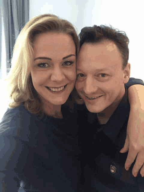 a man and a woman are posing for a picture and the man is wearing a black shirt with a shield on it