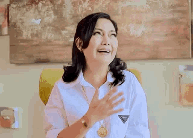 a woman in a white shirt is sitting in a yellow chair and laughing .
