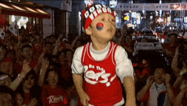 a young boy wearing a red jersey that says be the cats is dancing in front of a crowd .