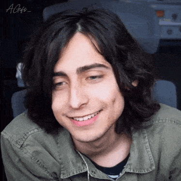 a young man with long hair is smiling and wearing a green shirt