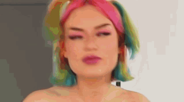 a woman with rainbow hair is making a funny face while standing in front of a white wall .