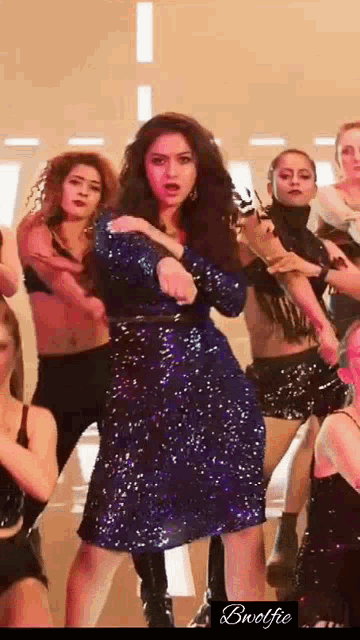 a woman in a blue sequined dress is dancing in front of a group of women .