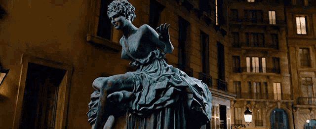 a statue of a woman in a long dress is sitting in front of a building