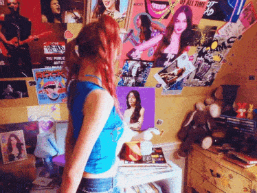 a girl stands in front of a wall covered in posters including one that says rock n roll