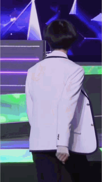 a man in a white suit stands on a stage with his back to the camera