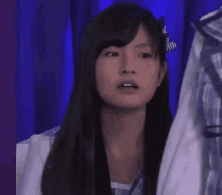 a woman with long black hair is standing in front of a blue curtain and a hanger .