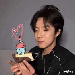 a man holding a piece of cake with a candle and a heart on it