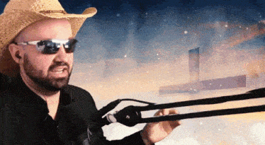 a man wearing a cowboy hat and sunglasses is holding a microphone in front of a cross