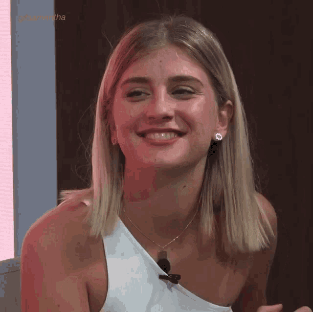 a woman wearing a white tank top and a necklace is smiling