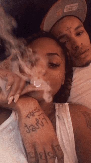 a man and a woman are smoking a cigarette and the woman has a tattoo that says jay