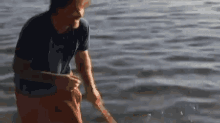a man in a blue shirt is standing in the water holding a stick .