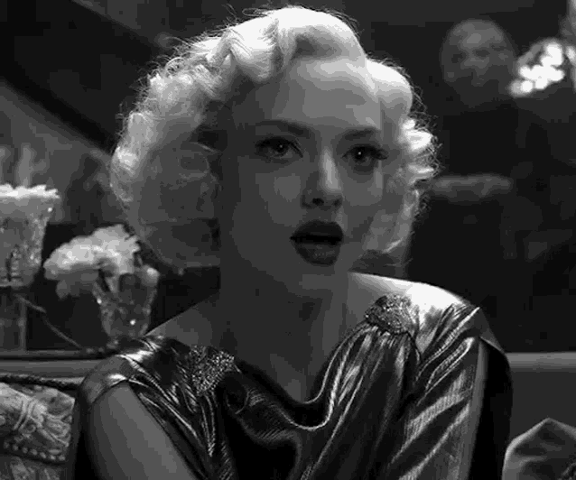 a black and white photo of a woman with blonde hair and a metallic dress .