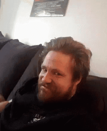 a man with a beard is sitting on a couch and making a funny face