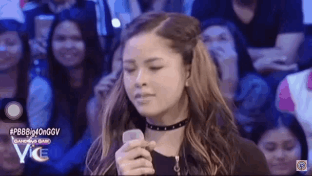 a young woman is holding a cell phone in front of a crowd .
