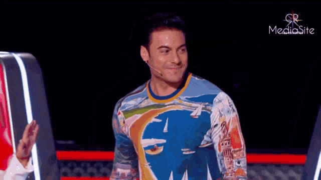 a man wearing a colorful shirt is standing in front of a microphone on a stage .