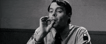 a man in a shirt and tie is smoking a cigarette .