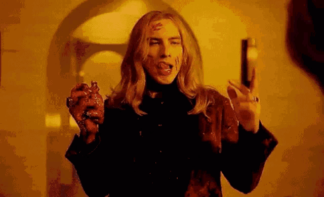 a man with long blonde hair is holding a bloody heart and a gun .