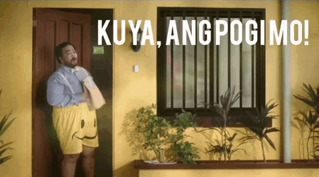 a man in a smiley face shorts stands in front of a yellow house