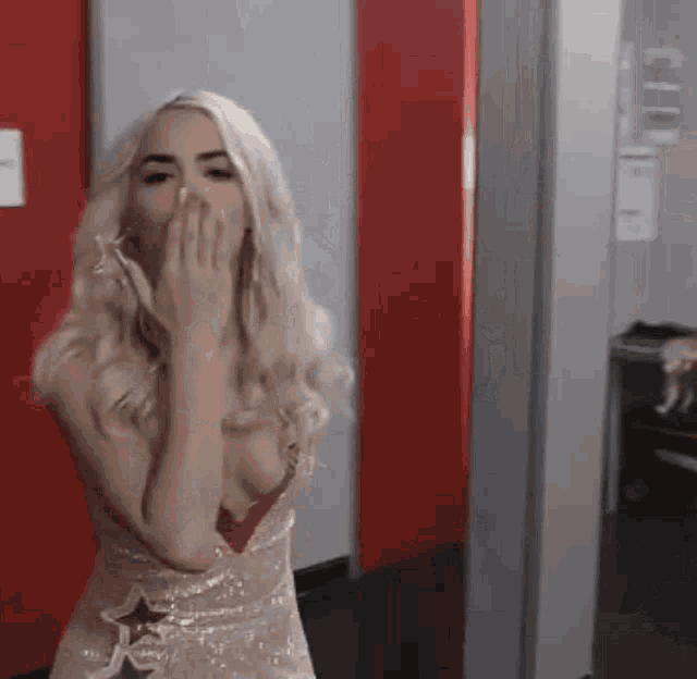 a blonde woman in a dress is covering her mouth with her hand .