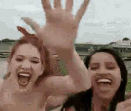 two women are laughing and waving their hands in the air while standing next to each other on a beach .