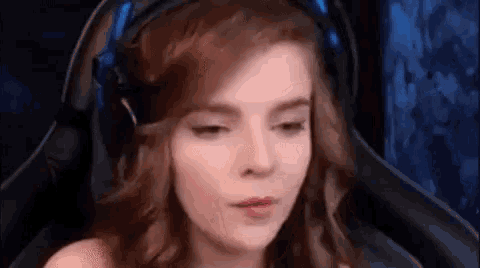 a woman wearing headphones is sitting in a gaming chair and making a funny face .