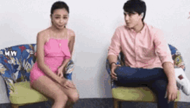 a man and a woman are sitting in chairs . the woman is wearing a pink dress .