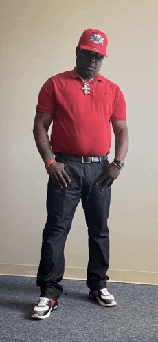 a man wearing a red polo shirt and a red hat with a lion on it is standing with his hands on his hips