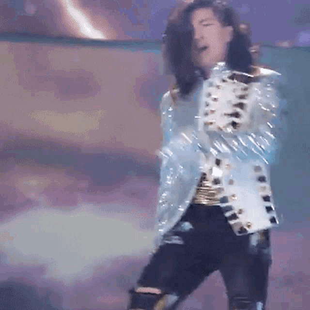 a man with long hair is dancing on a stage