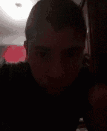 a close up of a man 's face in a dark room with a light coming from the ceiling .