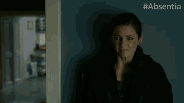 a woman leaning against a wall with #absentia on the bottom right