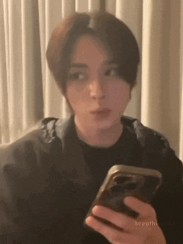 a young man is sitting on a couch holding a cell phone .