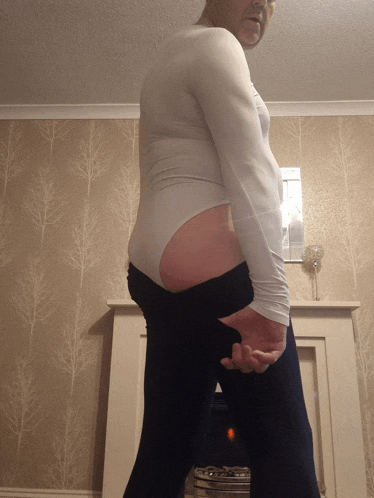 a man wearing a white leotard and black pants stands in front of a fireplace