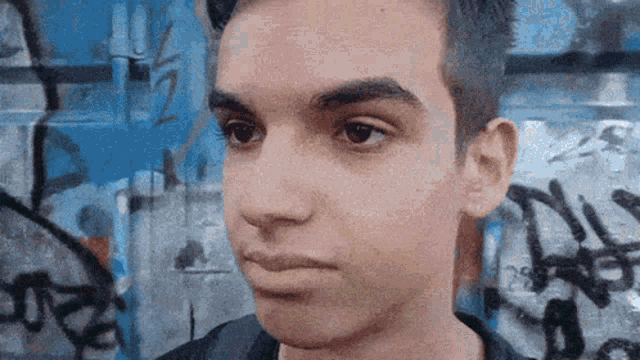 a close up of a young man 's face in front of a graffiti wall