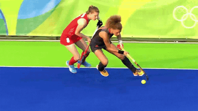 two female field hockey players are playing on a field