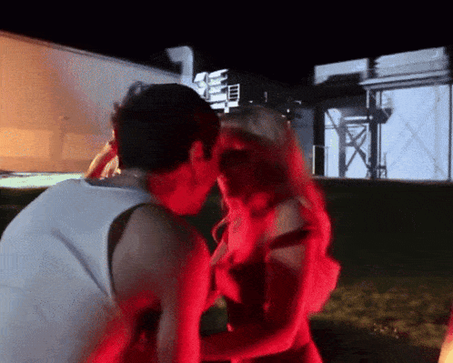 a man and a woman are kissing in front of a building that has the letter n on it