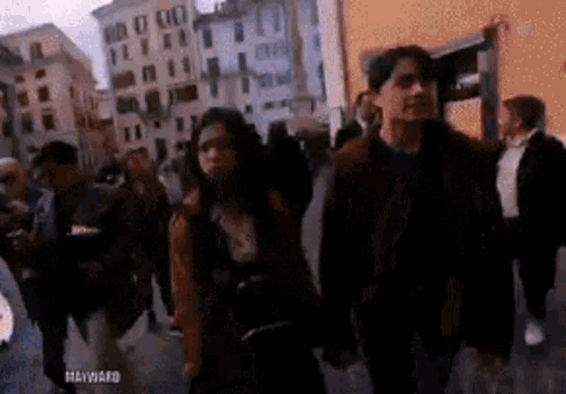 a man and a woman are walking down a city street holding hands .