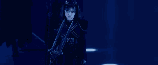 a woman in a black dress is standing in a dark room holding a sword .