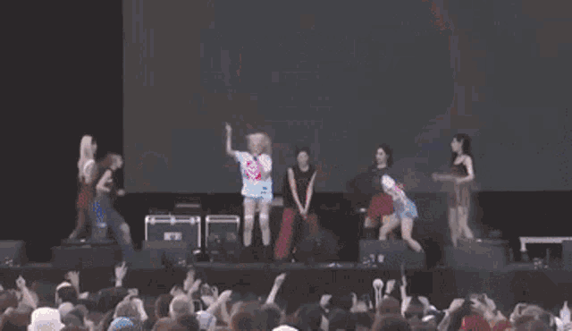 a group of people dancing on a stage in front of a large screen