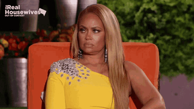 a woman in a yellow one shoulder dress is sitting in an orange chair with the words real housewives out of context behind her