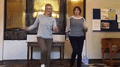 two women are dancing together in a room with a bulletin board in the background .