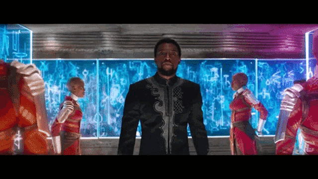 a man in a black suit stands in front of a group of people in red jumpsuits