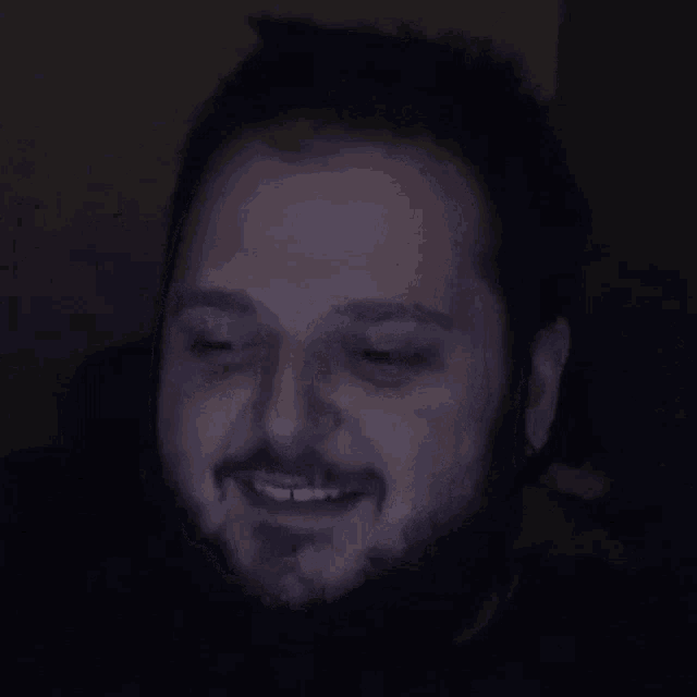 a man with a beard is screaming with his mouth open in the dark .