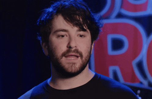 a man with a beard is standing in front of a large red letter r.