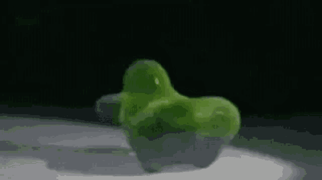 a green gummy penguin is sitting on a white surface .