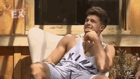 a man in a tank top is sitting on a chair with his hand on his chin