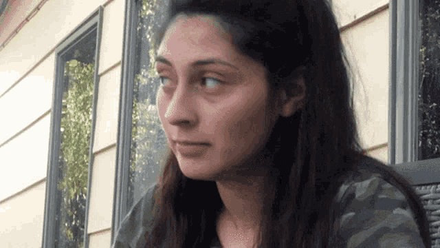 a woman in a camo shirt looks to the side