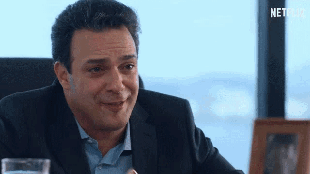 a man in a suit is sitting at a table with a glass of water and a netflix logo in the background
